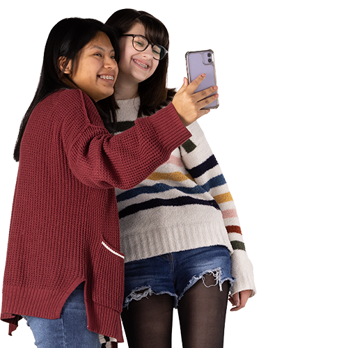 Two teenage girls huddled together taking a selfie and smiling.